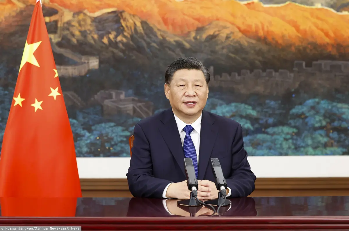 Xi Jinping siedzi w towarzystwie chińskiej flagi.
