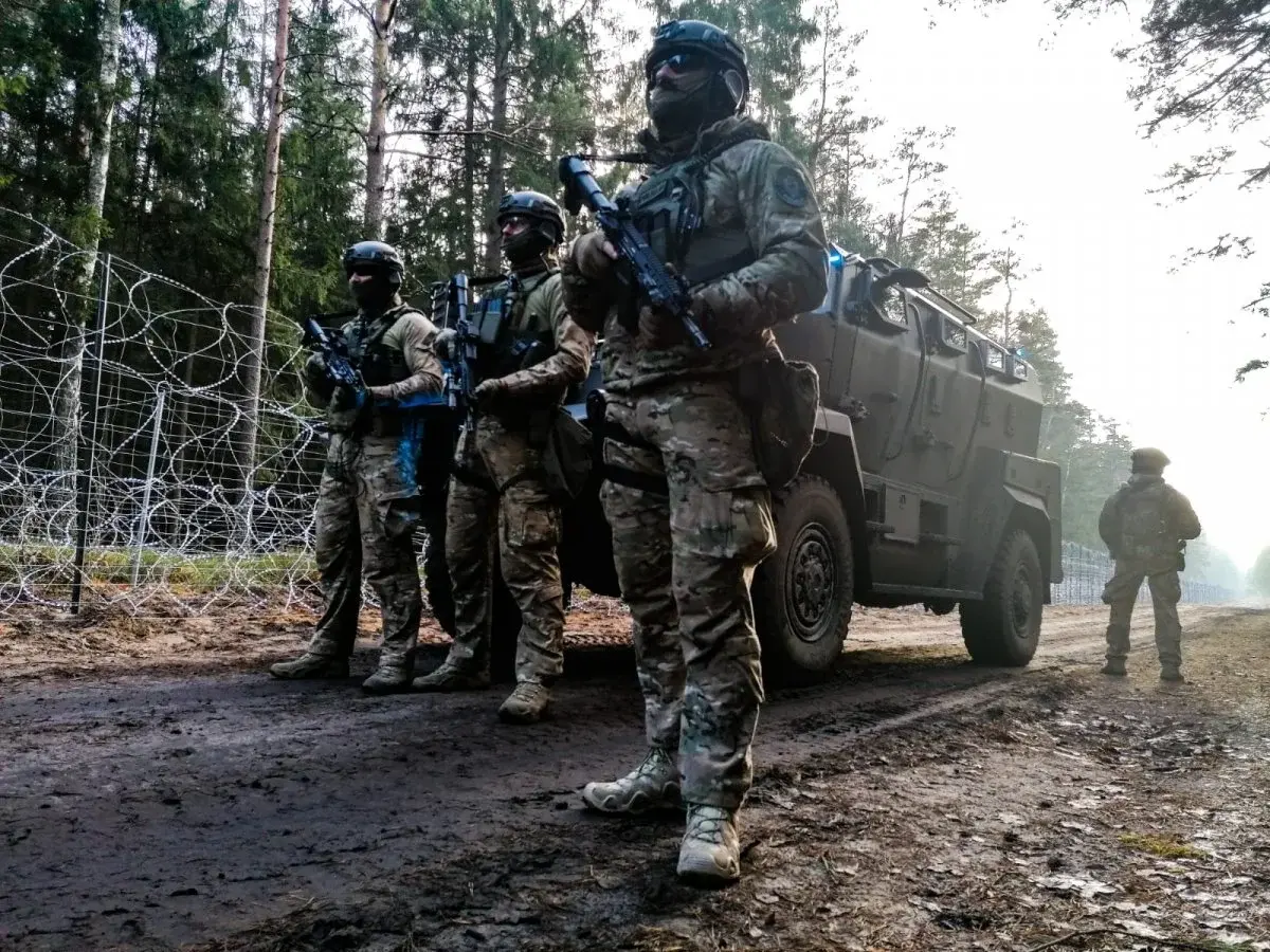 Grupa żołnierzy w uniformach bojowych przy wozie pancernym obok płotu granicznego