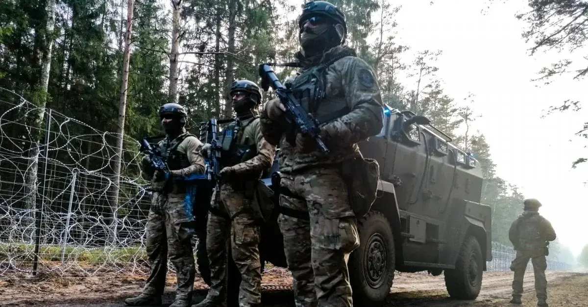 Grupa żołnierzy w uniformach bojowych przy wozie pancernym obok płotu granicznego