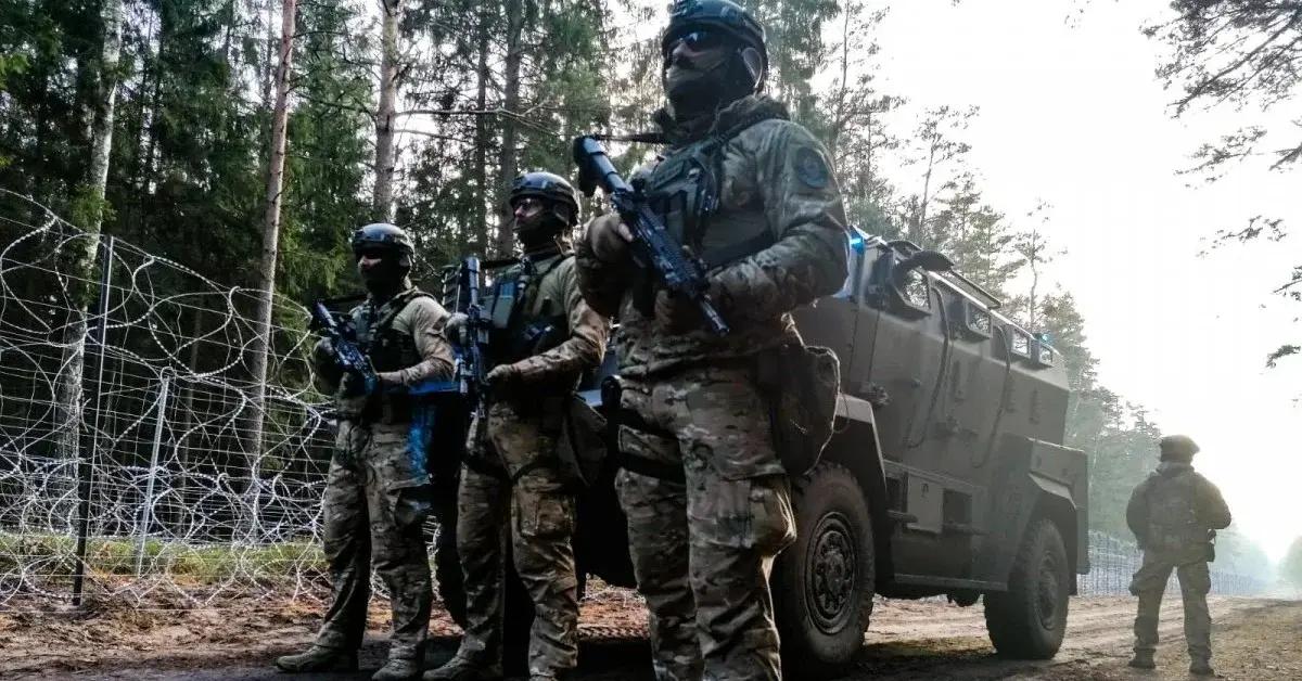 Grupa żołnierzy w uniformach bojowych przy wozie pancernym obok płotu granicznego