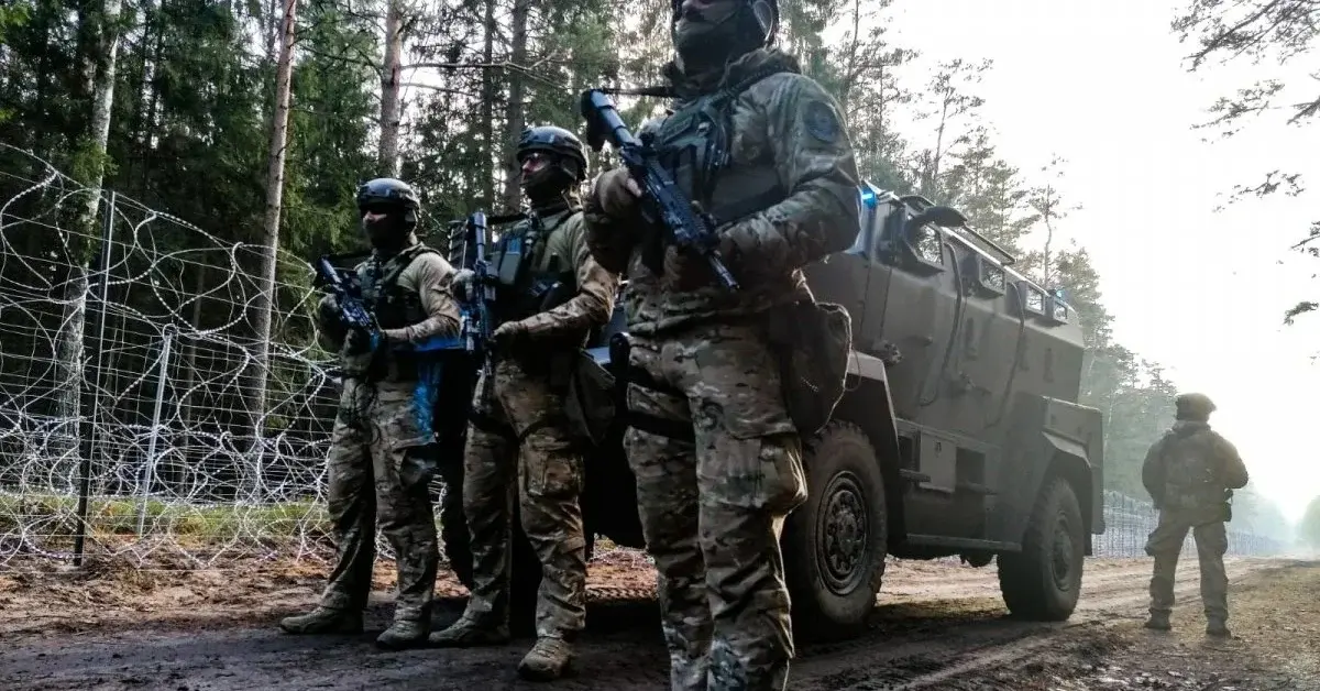 Grupa żołnierzy w uniformach bojowych przy wozie pancernym obok płotu granicznego