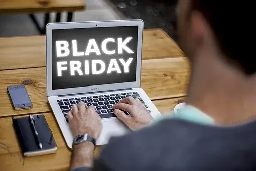 Mężczyzna trzyma dłonie nad klawiaturą, a na ekranie wyświetlony jest napis Black Friday