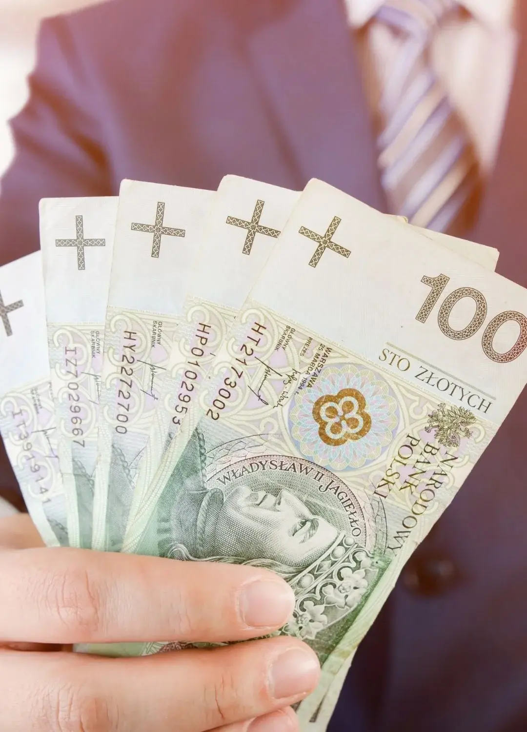 Mężczyzna w garniturze trzymający banknoty stuzłotowe