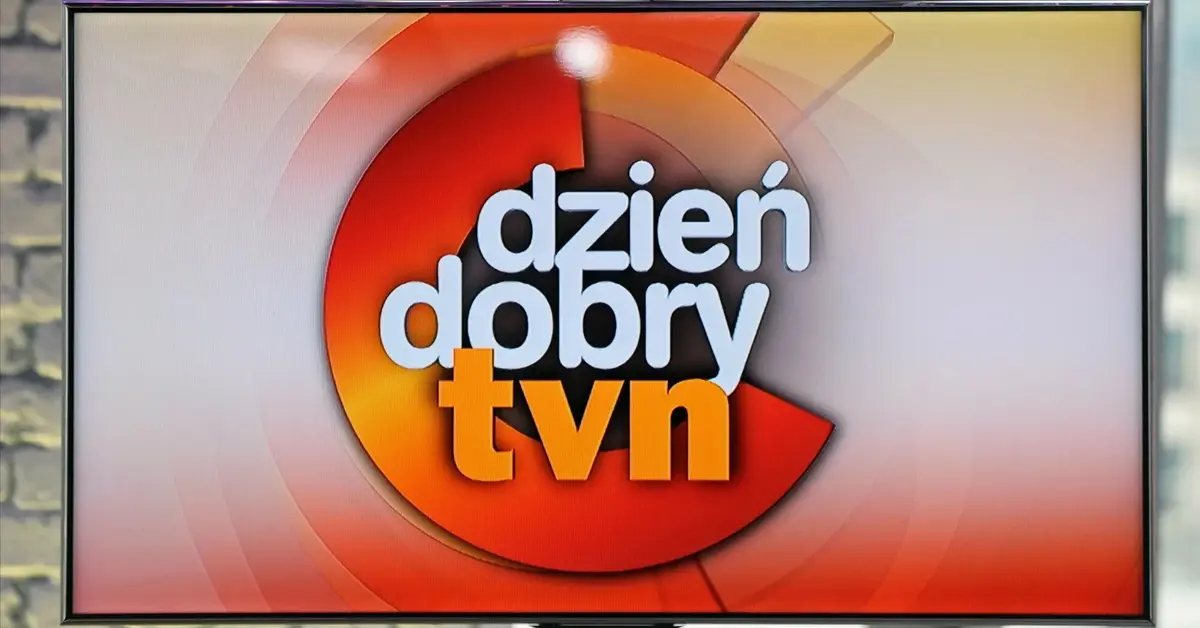 Biało-żółty napis "dzień dobry TVN" na czerwonym tle wyświetlony na telewizorze marki Samsung na tle ściany