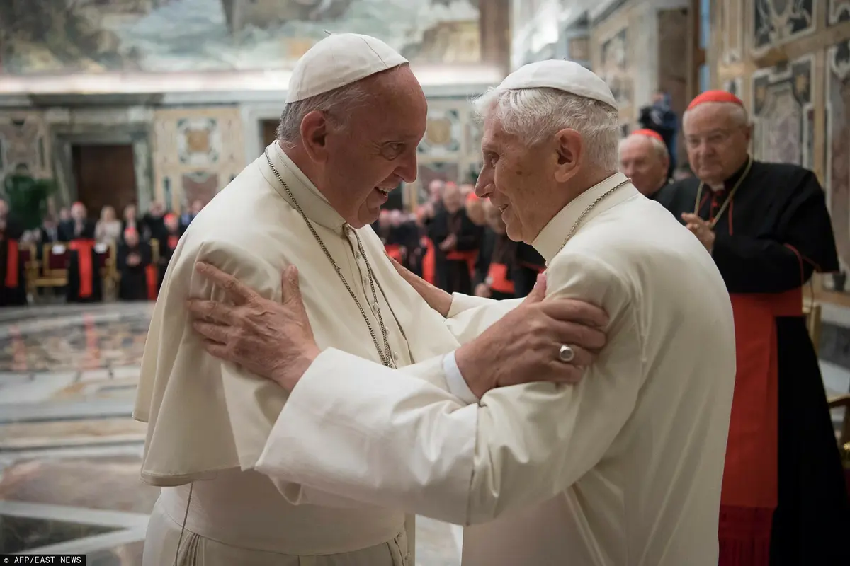 papież franciszek obejmuje się z papieżem benedyktem XVI w tle widać grupę arcybiskupów 