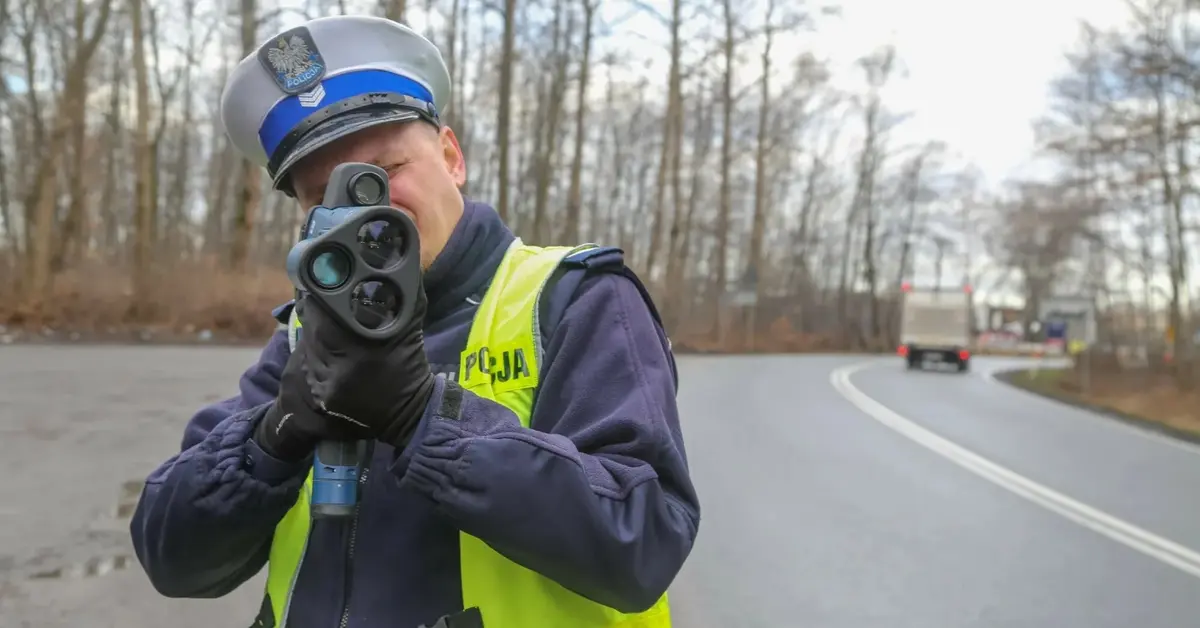 Policjant z fotoradarem stoi przy drodze i celuje w nadjeżdżający pojazd