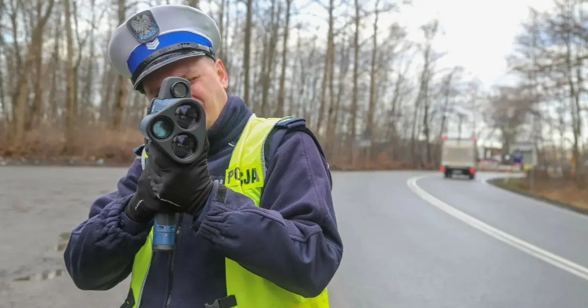 Policjant z fotoradarem stoi przy drodze i celuje w nadjeżdżający pojazd