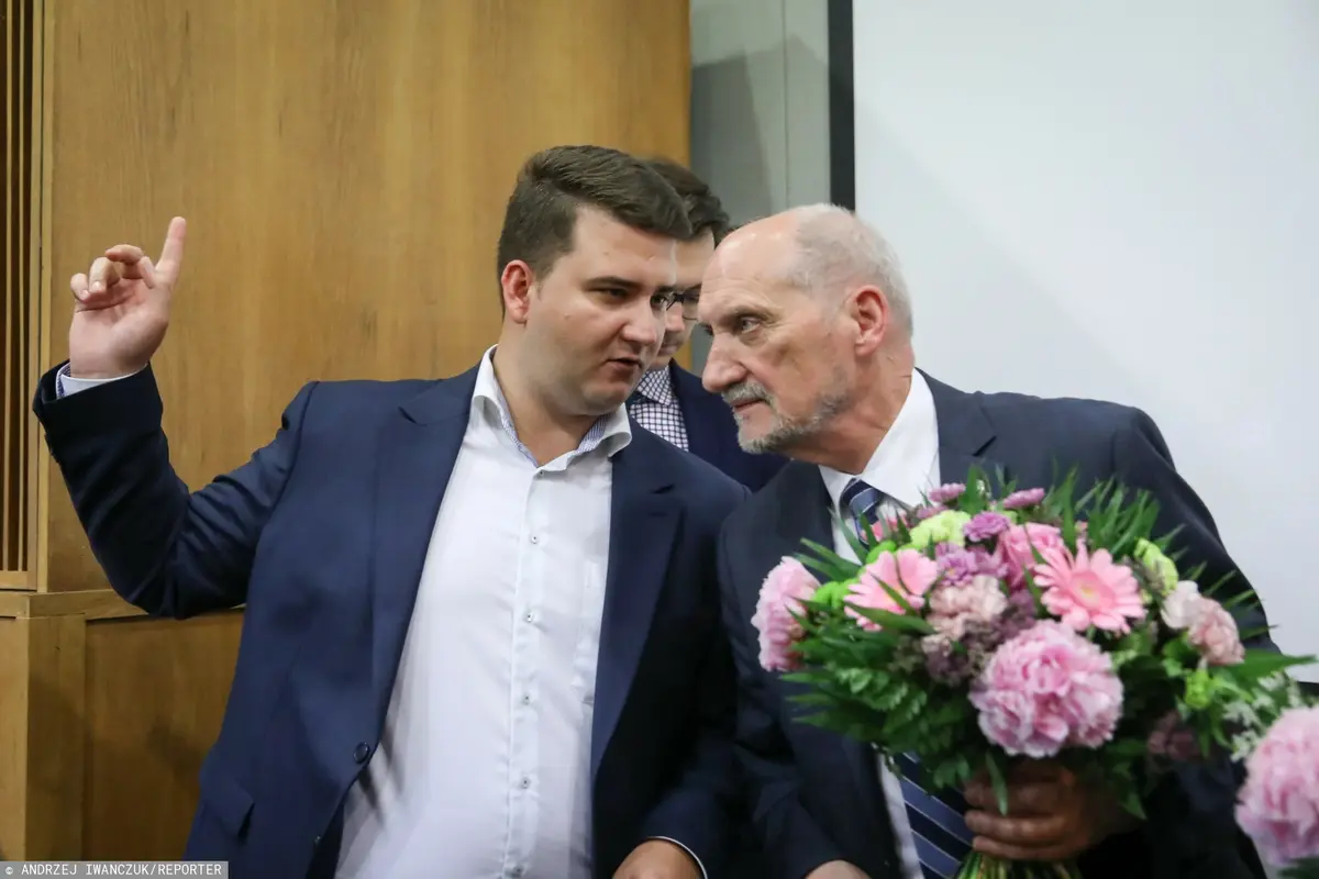 Bartłomiej Misiewicz pokazuje coś Antoniemu Macierewiczowi, który trzyma bukiet kwiatów 
