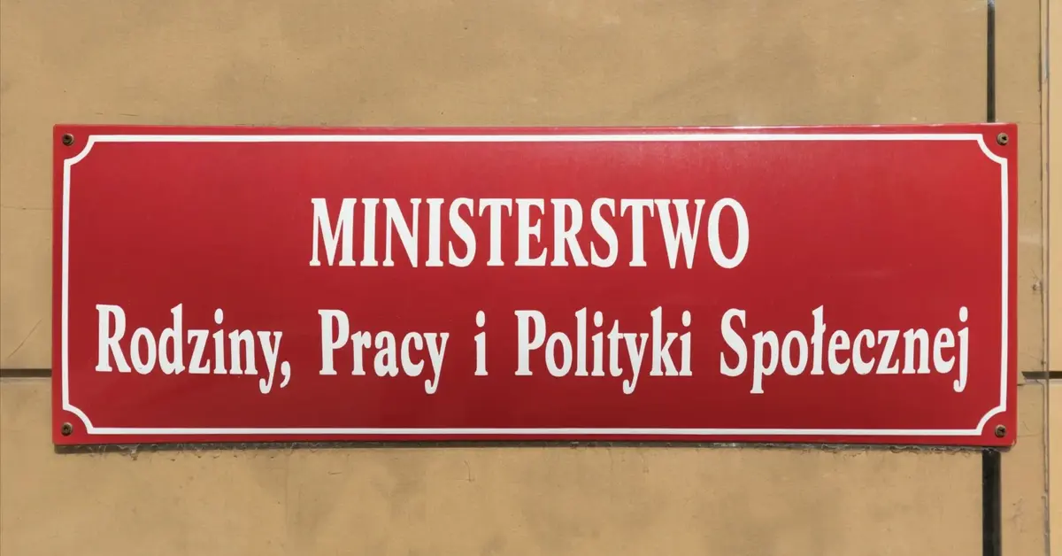 Czerwona tablica informacyjna Ministerstwa Rodziny, Pracy i Polityki Społecznej na tle jasnej ściany