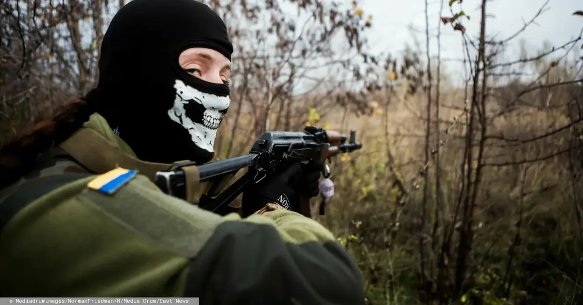 ukraiński żołnierz z maską z trupią czaszką na twarzy celuje z karabinu i patrzy w obiektyw