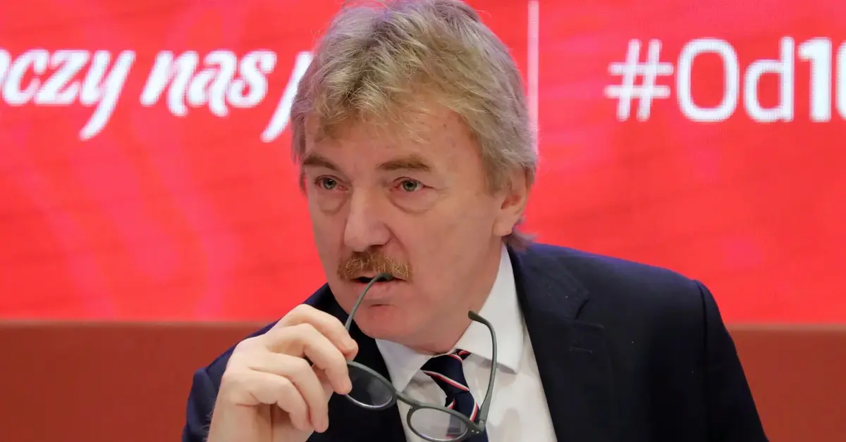 Zbigniew Boniek na czerwonym tle podczas konferencji prasowej przygryzający okulary