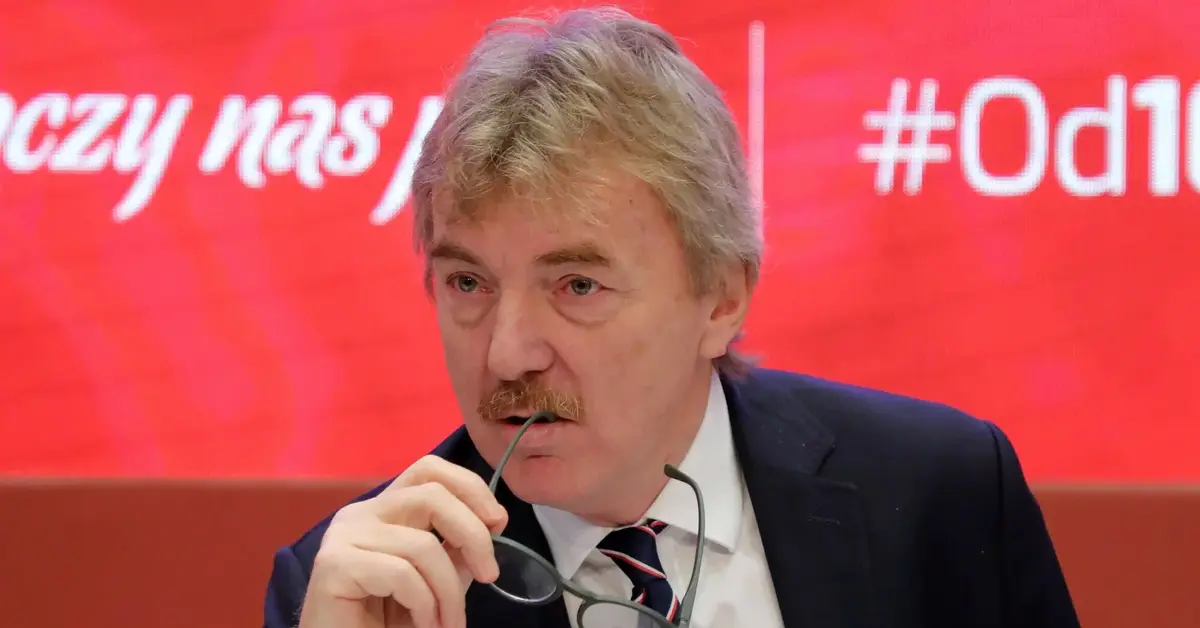 Zbigniew Boniek na czerwonym tle podczas konferencji prasowej przygryzający okulary