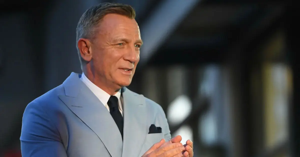 Daniel Craig w jasnym garniturze klaszcze w dłonie.