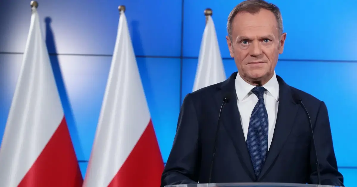 Donald Tusk podczas konferencji prasowej na tle polskich flag przy mównicy z logiem PO 