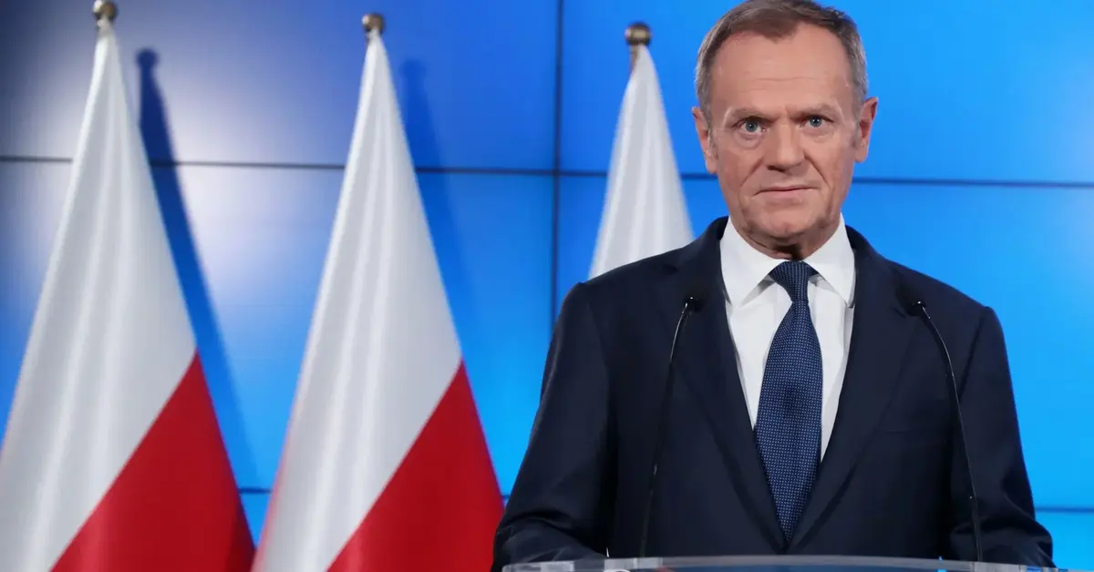 Donald Tusk podczas konferencji prasowej na tle polskich flag przy mównicy z logiem PO 