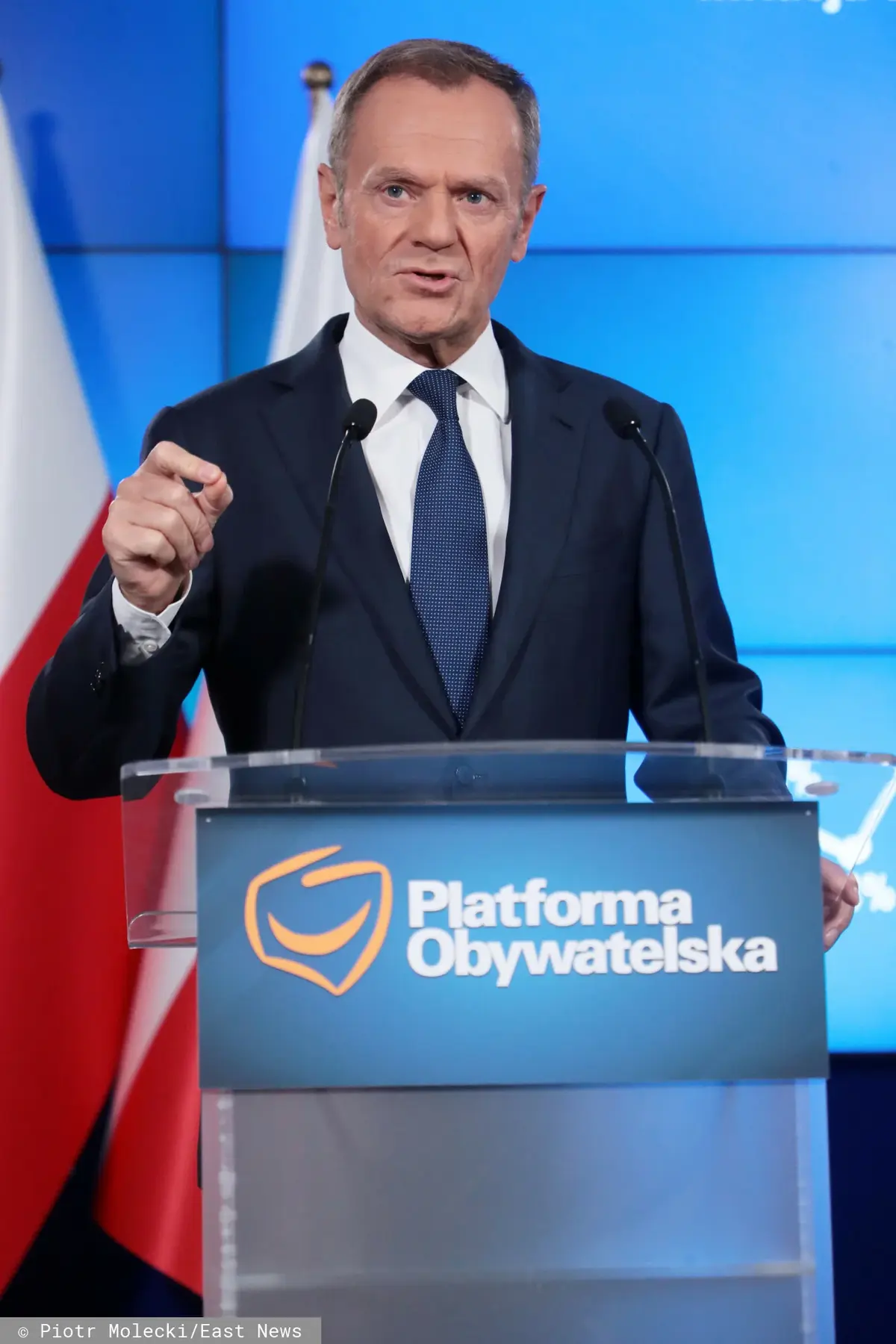 Donald Tusk na konferencji prasowej za mównicą z logo PO