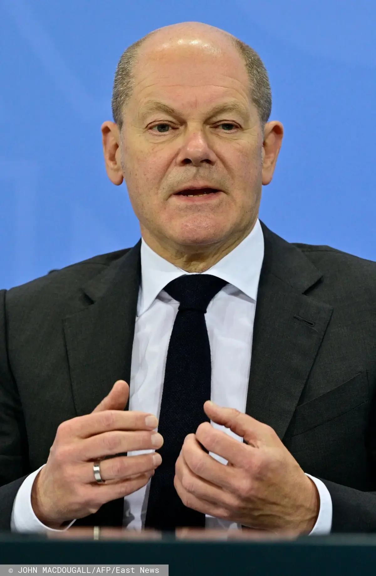 Olaf Scholz w garniturze i białej koszuli na niebieskim tle