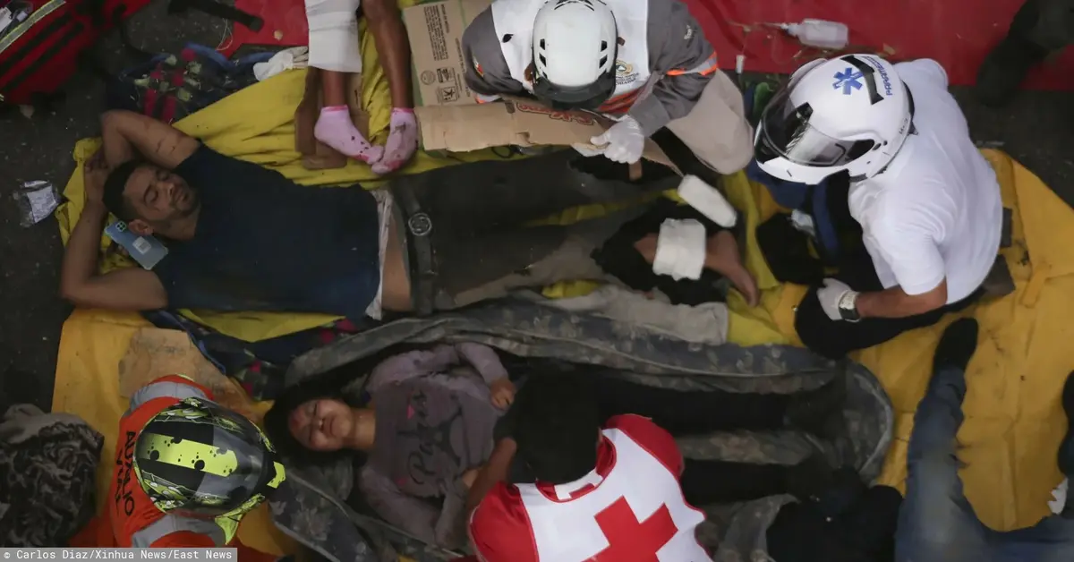 Ranny mężczyzna leżący na drodze w tłumie innych rannych w którym są sanitariusze udzielający pomocy