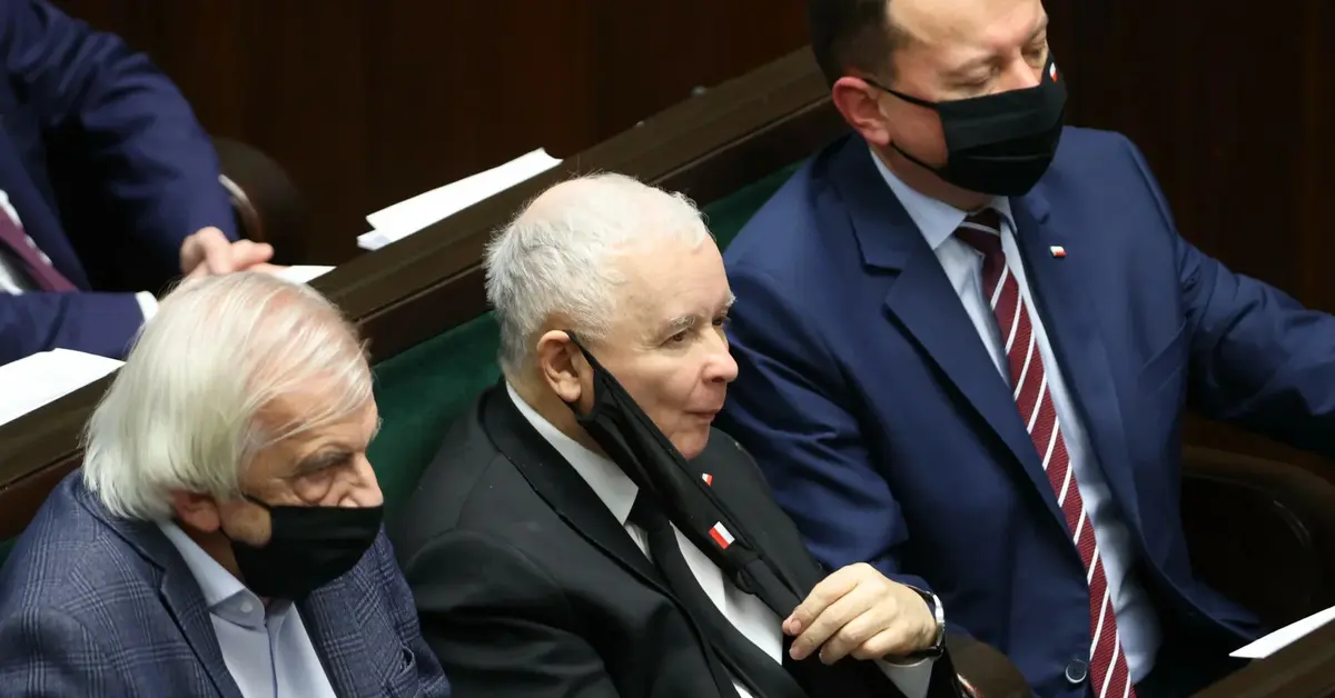 Jarosław Kaczyński ze ściągniętą maseczką siedzi w towarzystwie dwóch posłów na sejm RP.