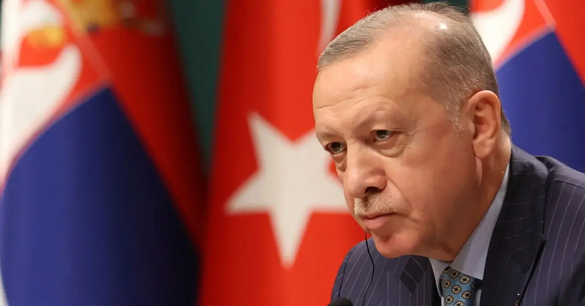 erdogan przed mikrofonem z groźną miną na tle tureckiej flagi