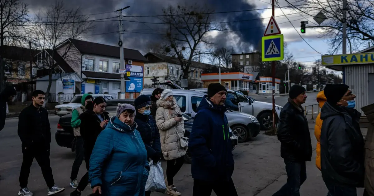 tłum ludzi w kijowie na ulicy, w tle dymy z pożaru po bombardowaniu