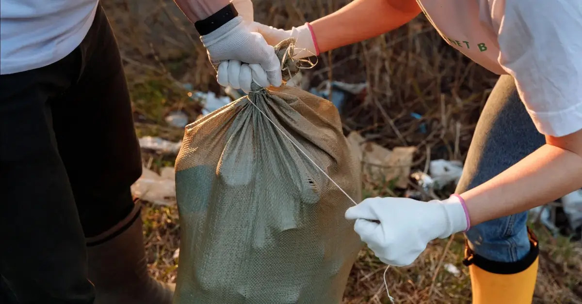 Dwoje ludzi zbiera śmieci nad rzeką i pakuje je do worka