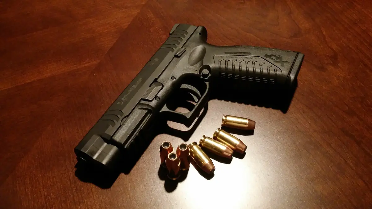 Czarny pistolet leżący na podłodze a obok niego kilka pocisków
