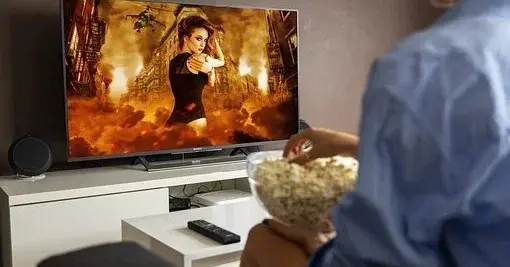 Mężczyzna ogląda telewizję, a w rękach ma miskę z popcornem