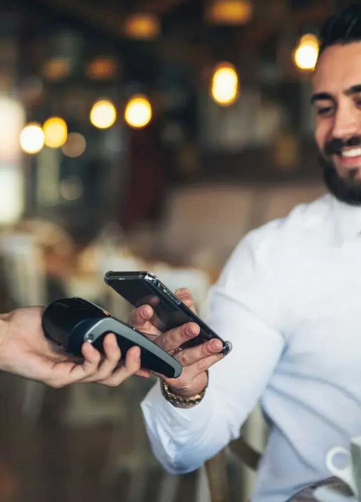 Uśmiechnięty mężczyzna w białej koszuli trzymający smartfon nad terminalem płatniczym