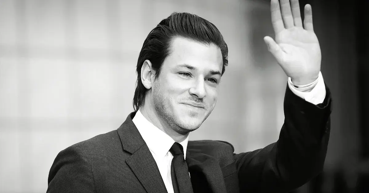 Gaspard Ulliel w garniturze macha ręką.