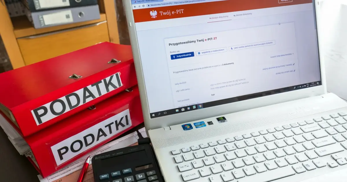 Komputer z zeznaniem podatkowym na ekranie i czerwone segregatory z podatkami