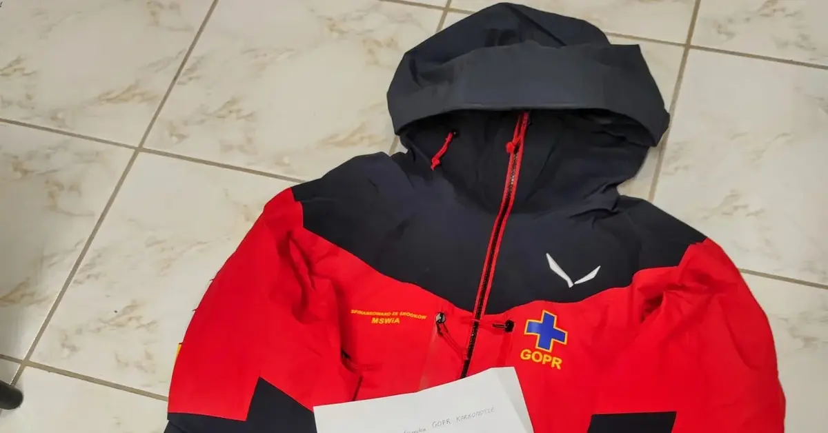 Czarno-czerwona kurtka ratownika GOPR leżąca na podłodze a na niej list na kartce