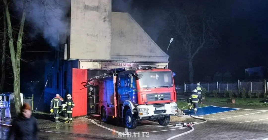 Zniszczony wóz strażacki obok palącej się remizy