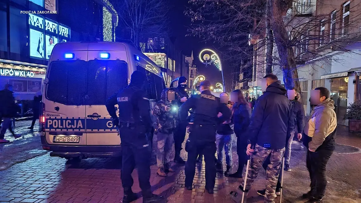 grupa osób stoi i dyskutuje z policją przy radiowozie stojącym na Krupówkach