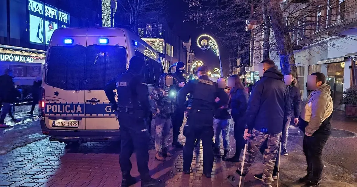 grupa osób stoi i dyskutuje z policją przy radiowozie stojącym na Krupówkach