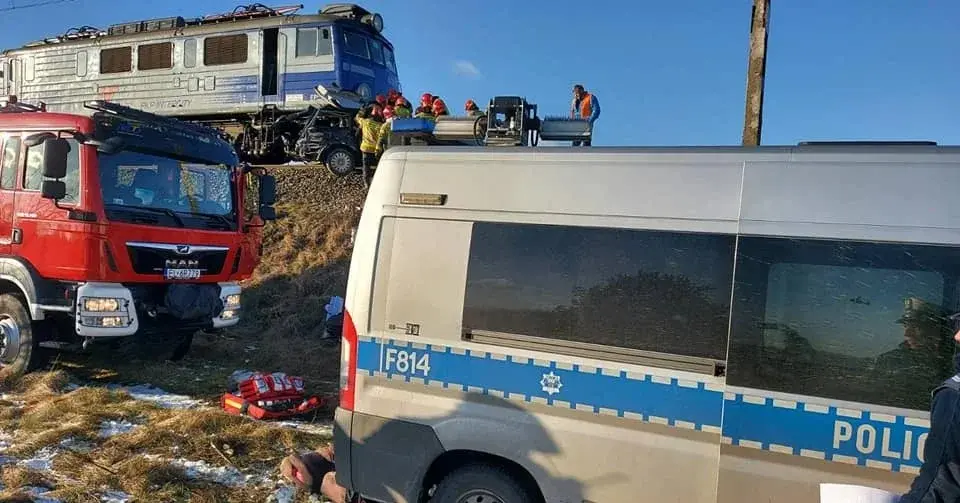 policyjny radiowóz i wóz straży obok pociągu, który uderzył w samochód osobowy