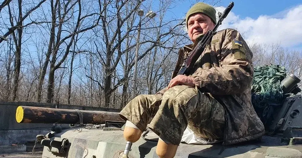 żołnierz bez nóg, z protezami, siedzi z karabinem na czołgu