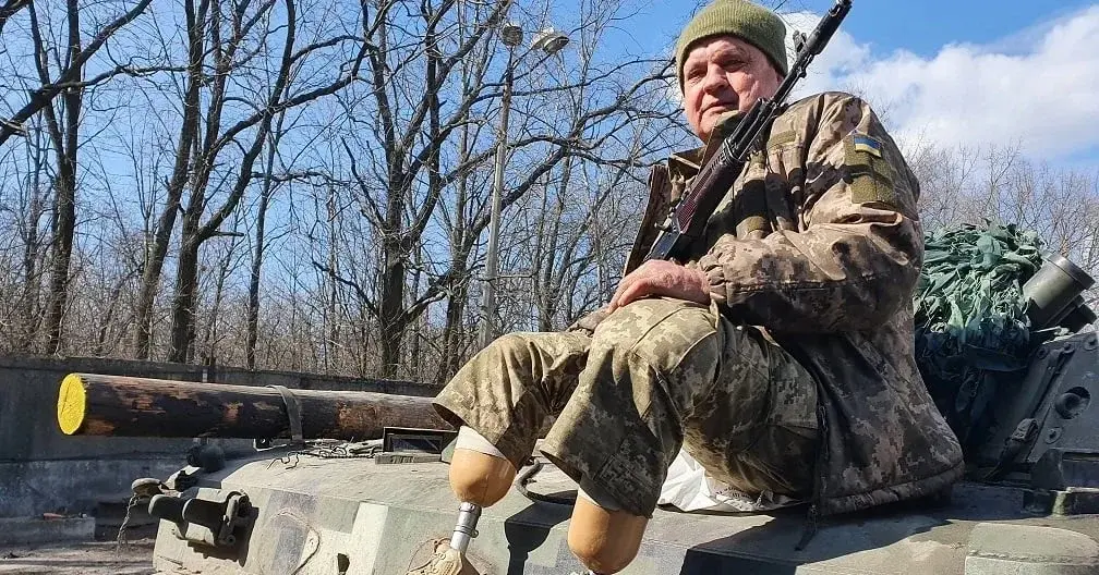 żołnierz bez nóg, z protezami, siedzi z karabinem na czołgu