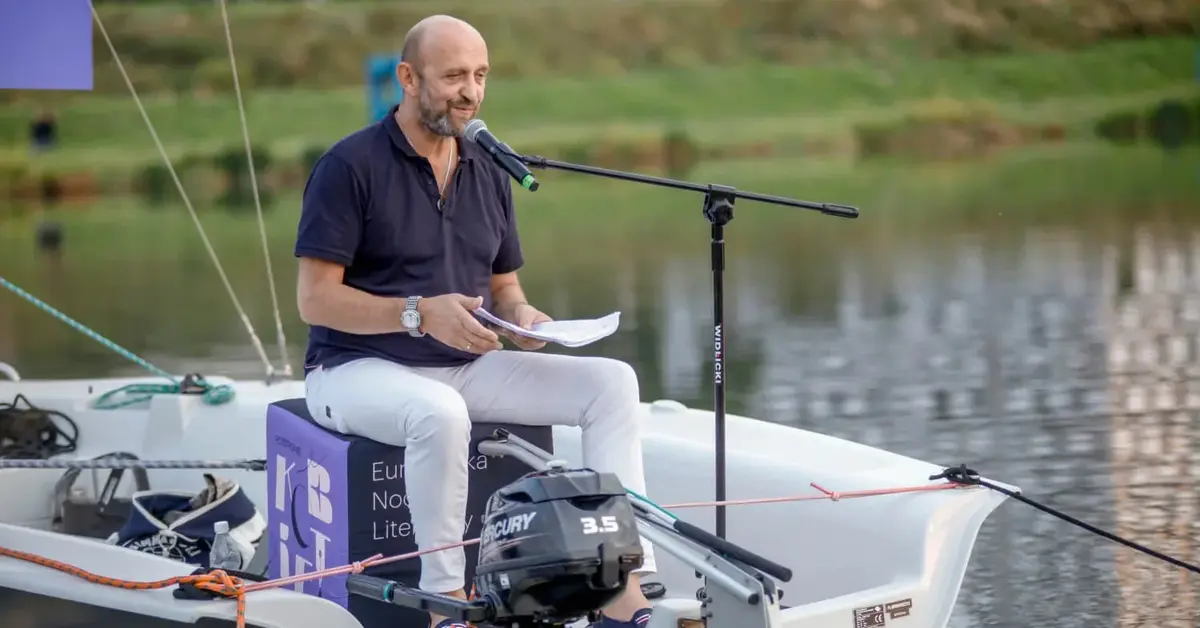 Janusz Chabior siedzi na łódce i mówi do mikrofonu.