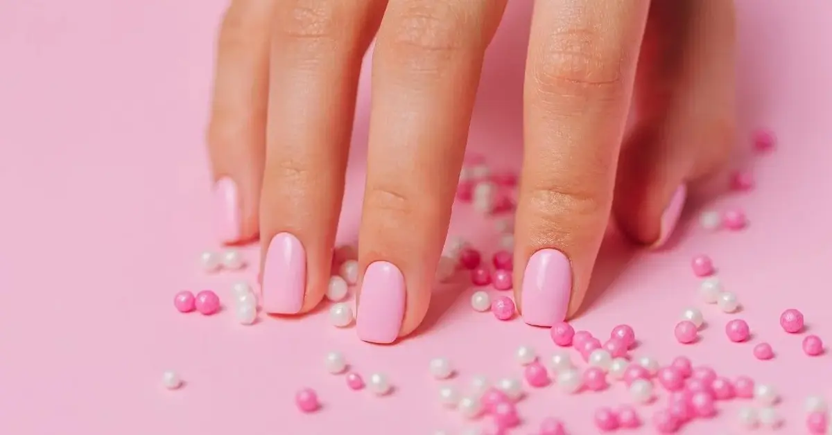 Na różowym tle kobieca dłoń z manicure akrylożele w kolorze różowym