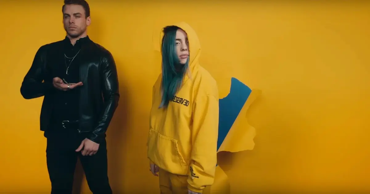 Billie Eillish w żółtej bluzie obok mężczyzny.