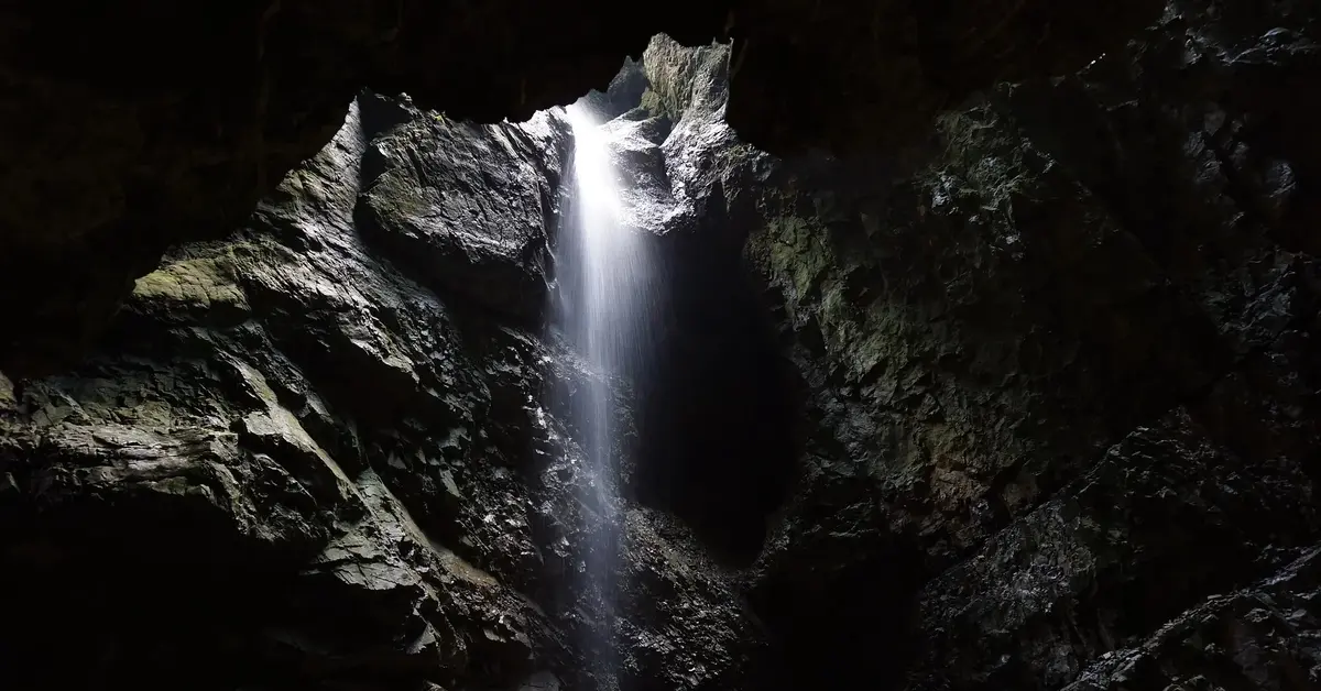 mroczna jaskinia do której z góry, wraz ze światłem, wpływa woda