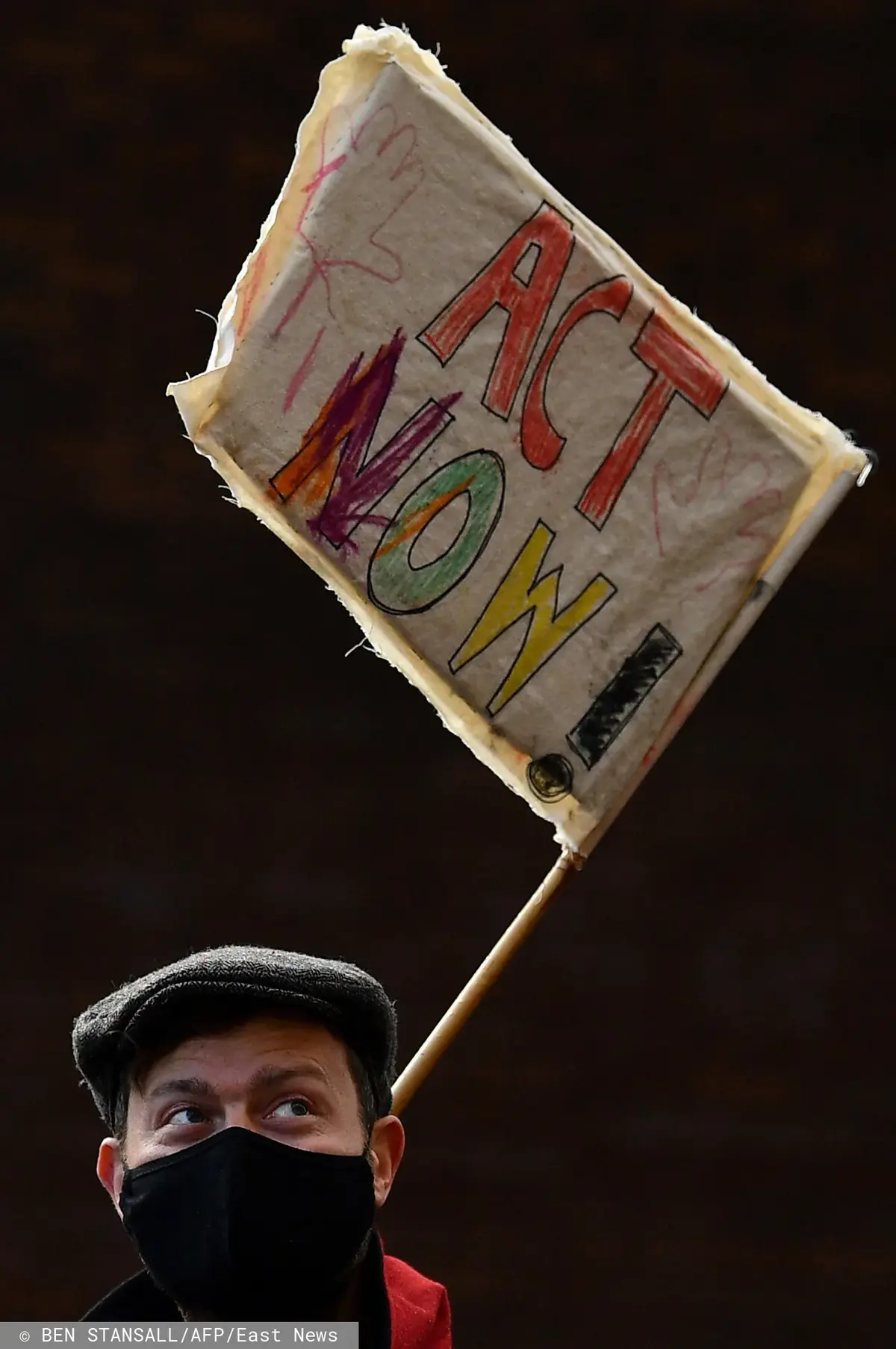 Mężczyzna demonstrujący podczas COP26 z napisem ACT NOW