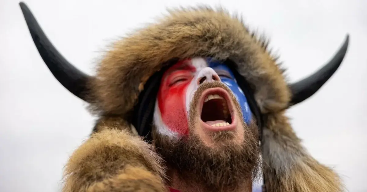 Mężczyzna w futrzanej czapce z rogami bizona wydaje okrzyk na tle nieba