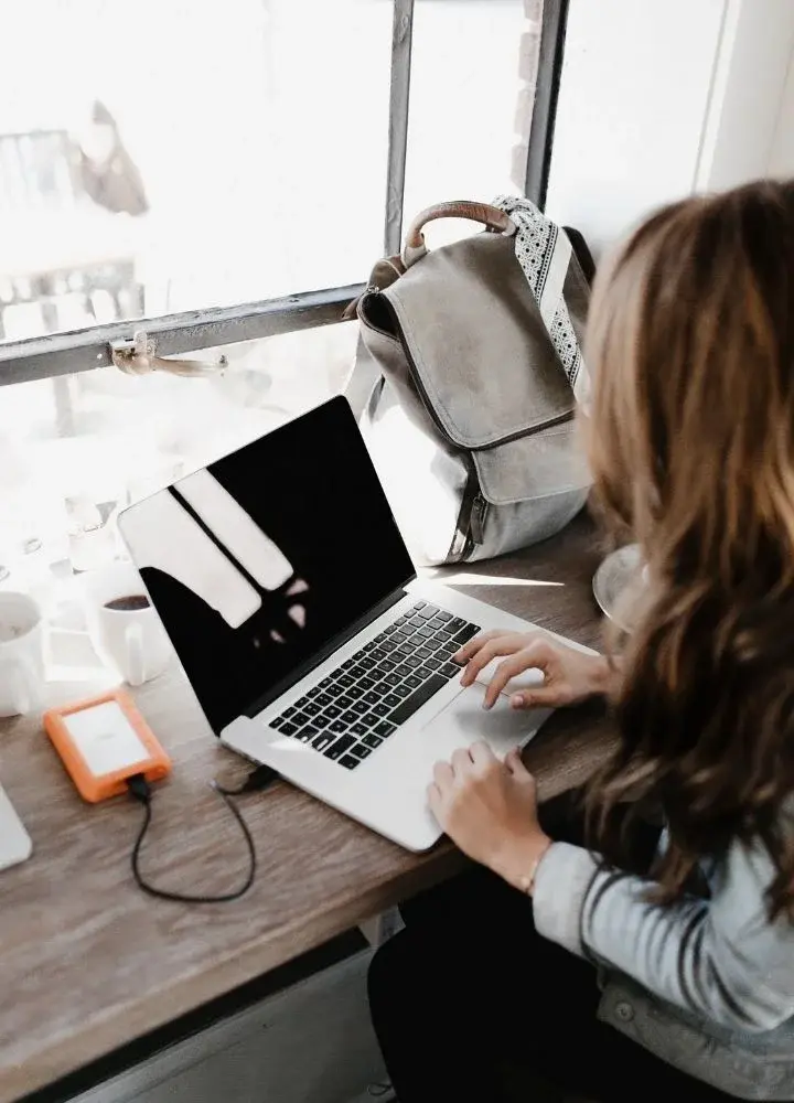 Kobieta zwrócona przodem do okna siedząc przy biurku z otwartym laptopem