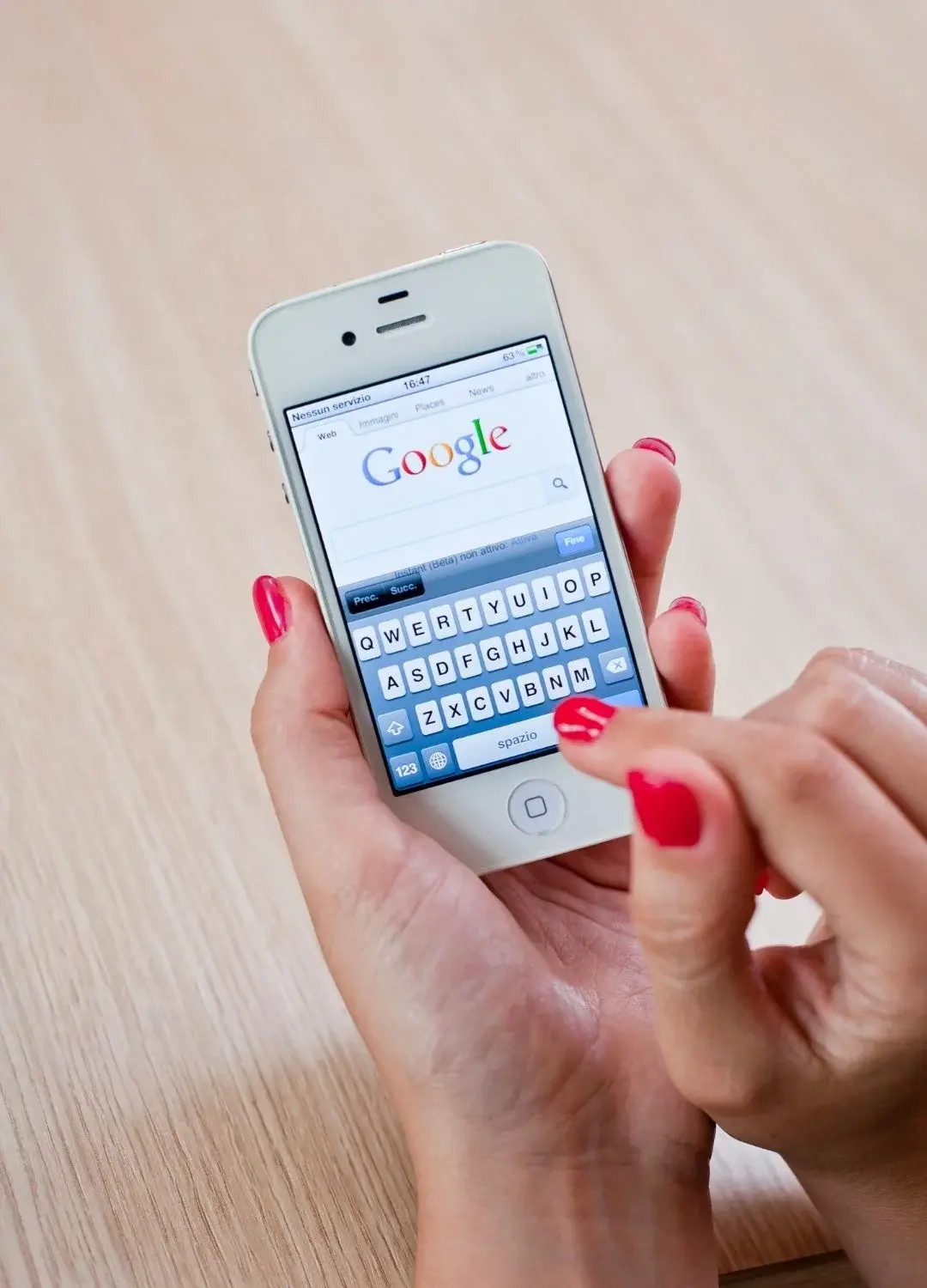 Kobiece dłonie z czerwonymi paznokciami trzymające smartfona z uruchomioną przeglądarką Google