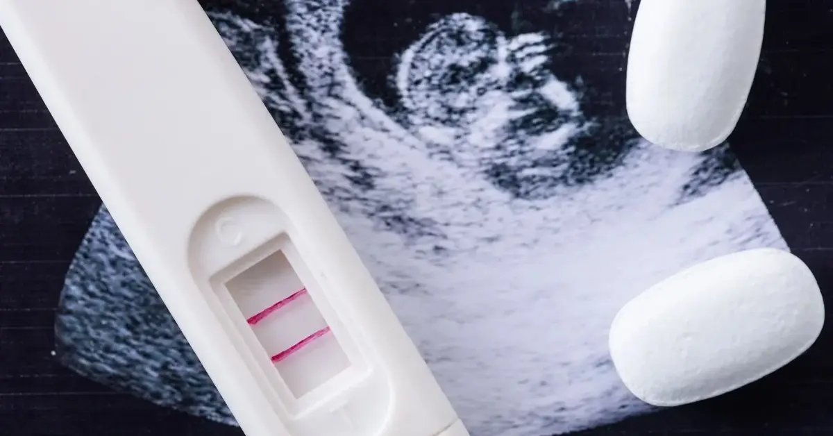 Pozytywny test ciążowy i dwie białe tabletki na zdjęciu USG płodu