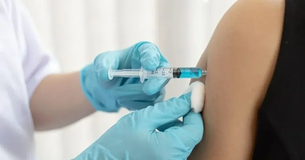 Ręce w błękitnych rękawiczkach wstrzykujące szczepionkę w ramię