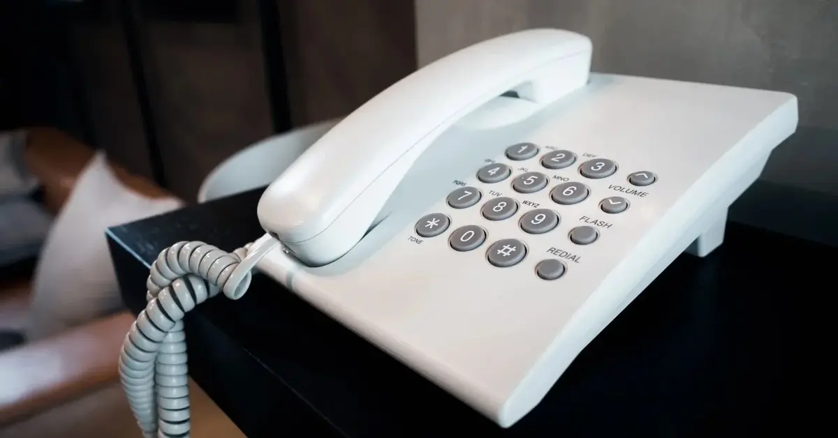 Biały telefon stacjonarny na czarnym stoliku