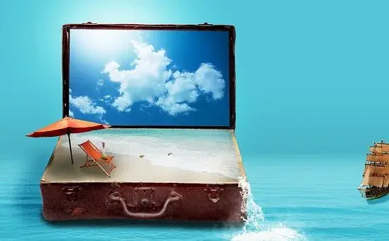 Laptop postawiony na walizce, a na ekranie laptopa widać chmury